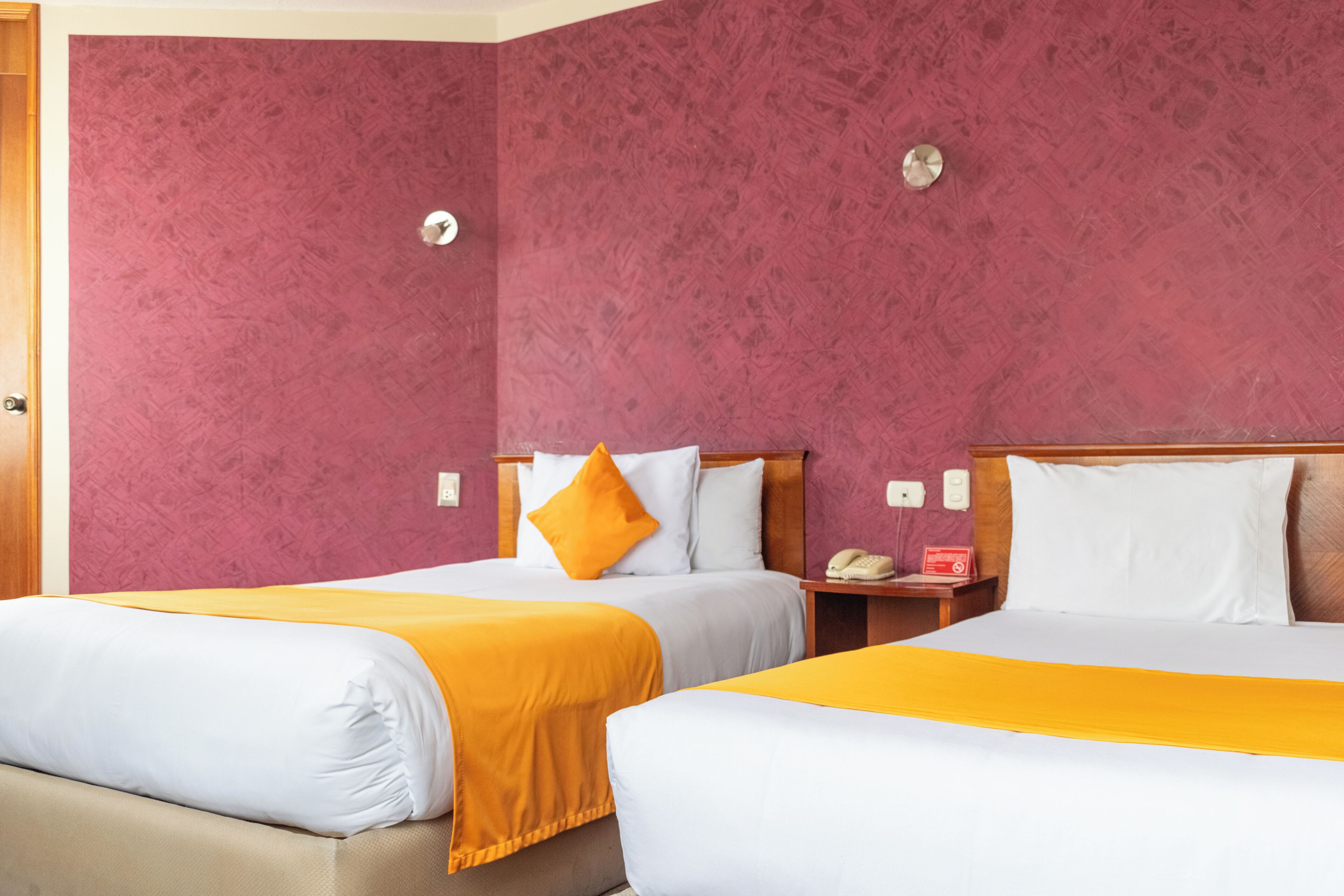 Ett hotellrum med två sängar, där varje säng har vita och orange sängkläder och en sänggavel i trä.