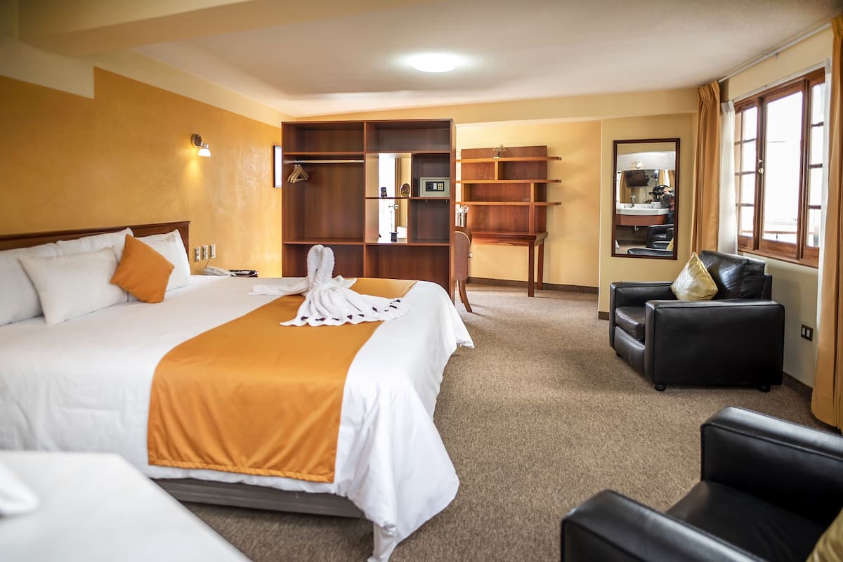 A hotel room with a large bed, a desk, a chair, and a wardrobe.