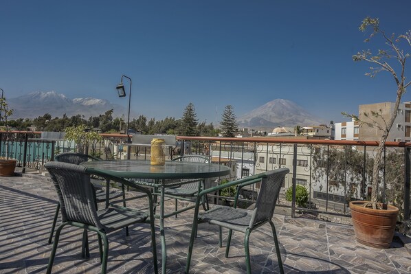 A terrace with a round table and chairs, a potted plant, and a view of mountains in the background.