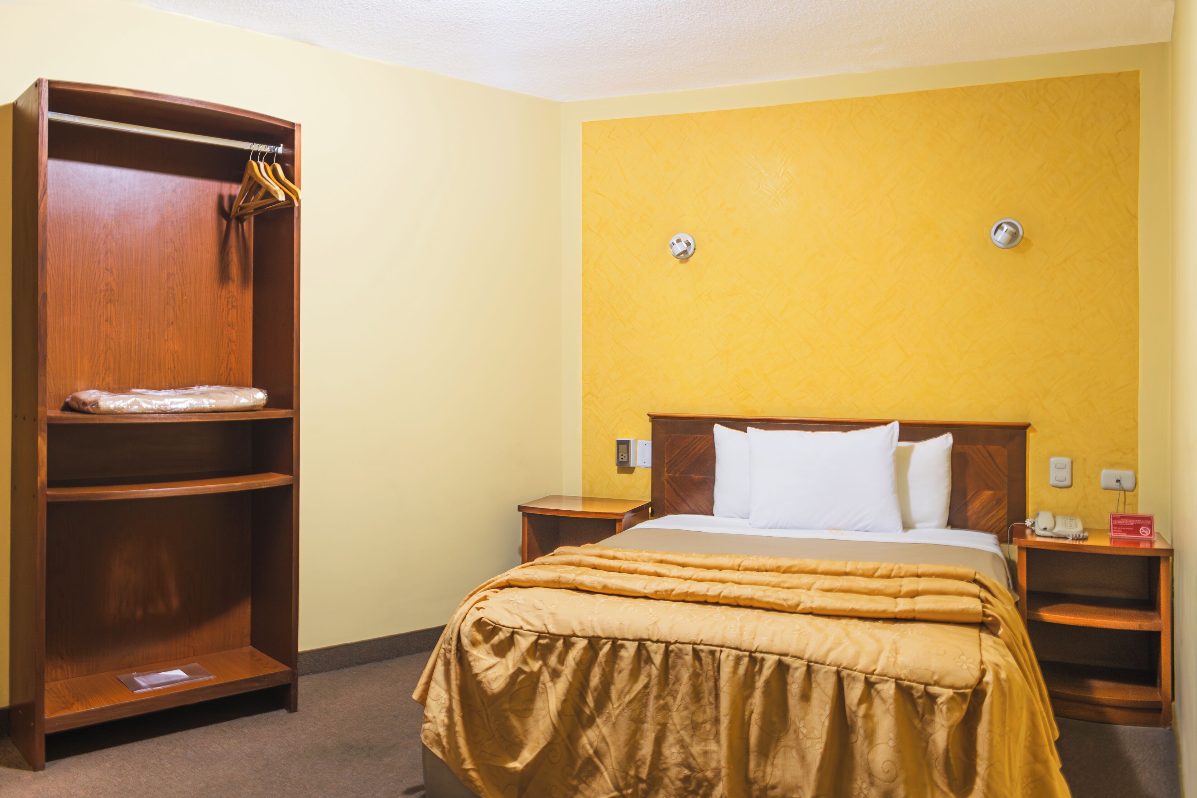 A hotel room with a bed, a wooden wardrobe, and a nightstand.