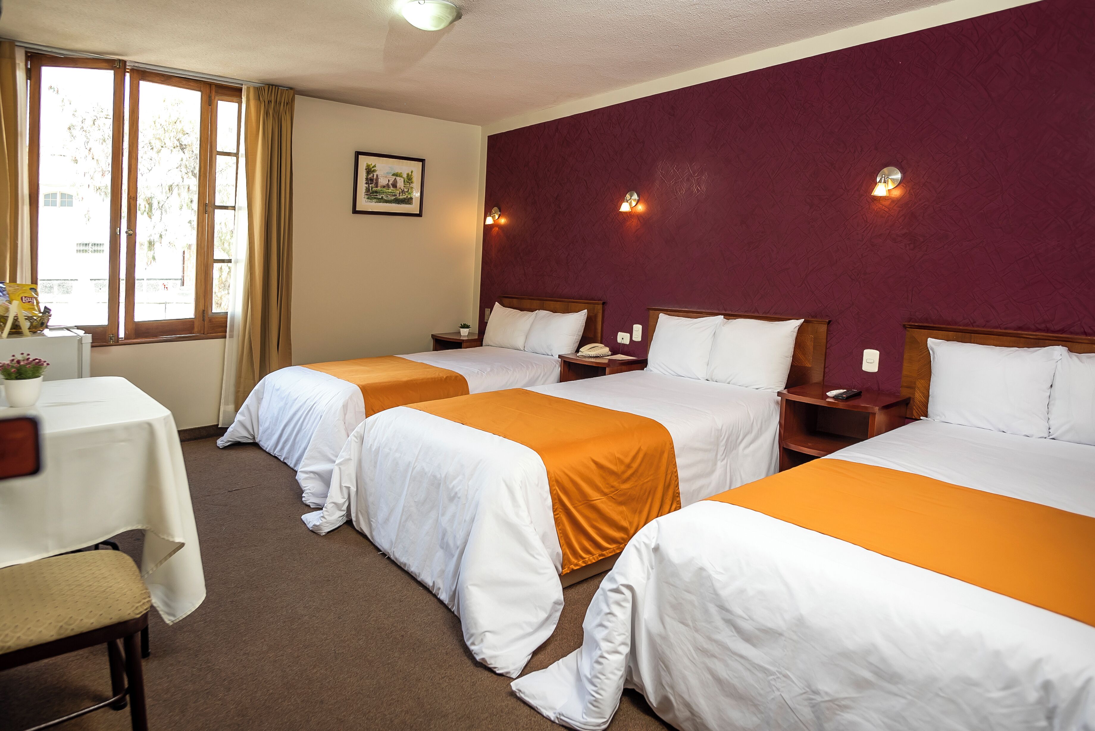 Habitación de hotel con tres camas, un escritorio y una ventana con cortinas.