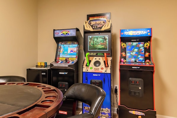 Une pièce comprenant trois bornes d’arcade, une table et une chaise.