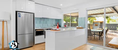 A modern kitchen with white cabinetry, a stainless steel refrigerator, and a large island with a glass top.