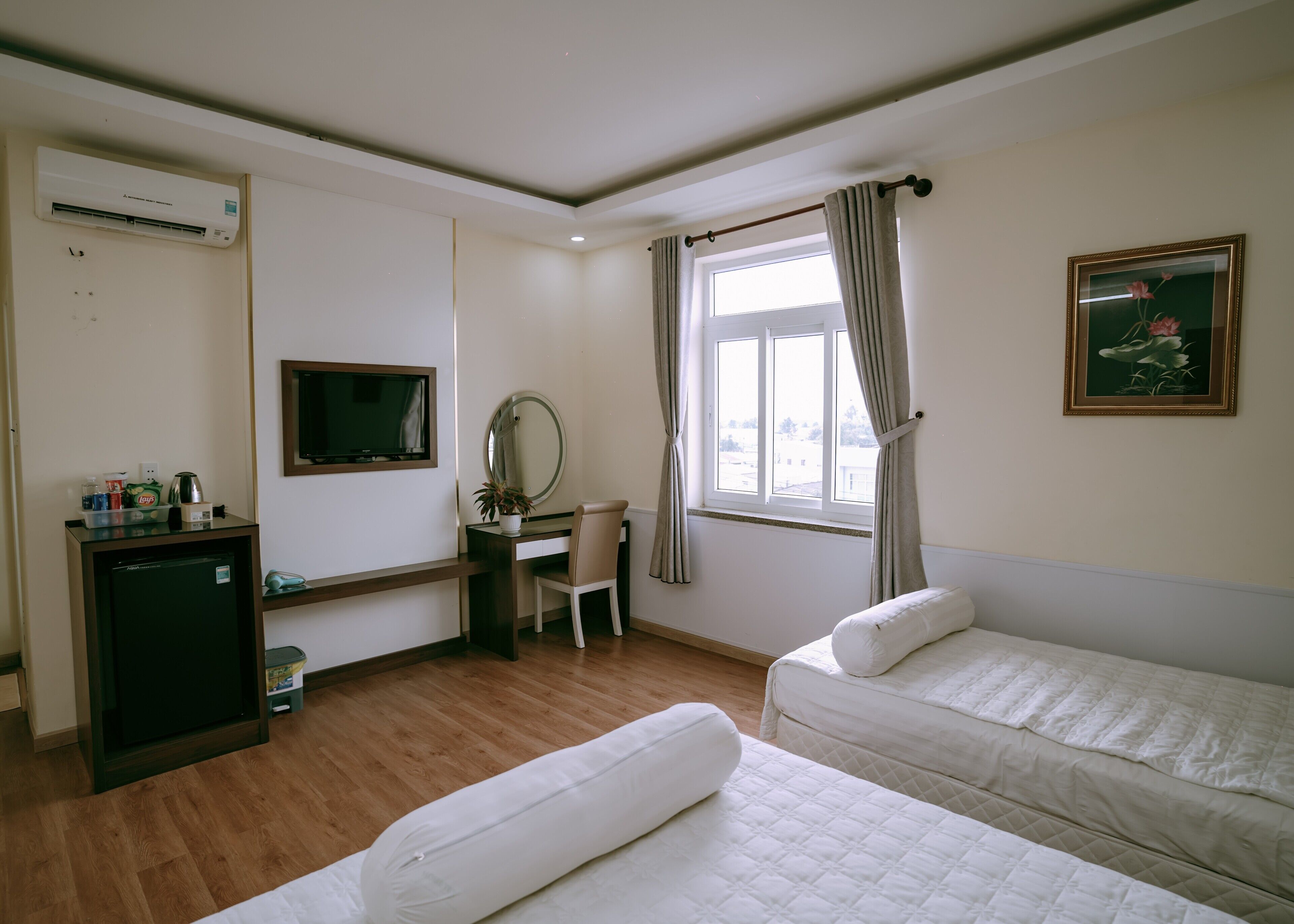 A hotel room with a desk, chair, two beds, a TV, and a window with curtains.