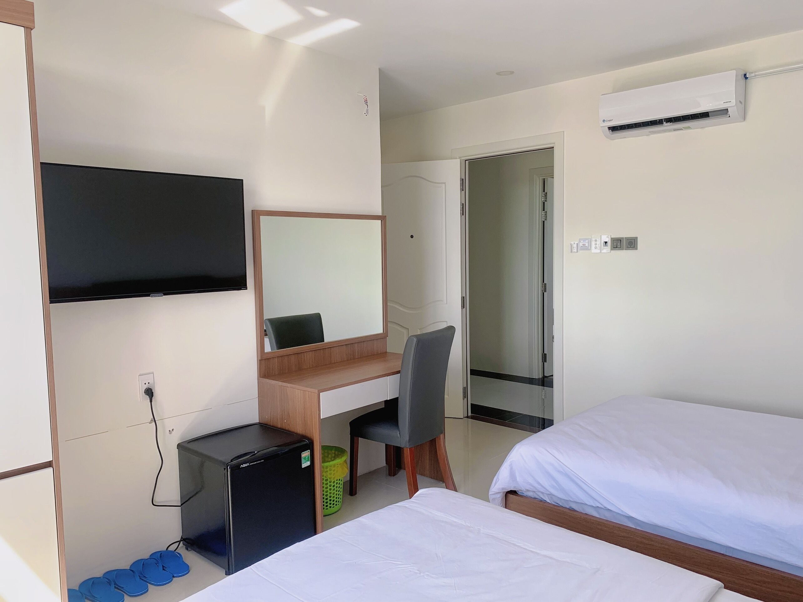 Een hotelkamer met een bureau, stoel, twee bedden, een televisie en een airconditioner.