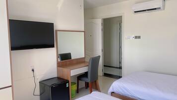 Een hotelkamer met een bureau, stoel, twee bedden, een televisie en een airconditioner.