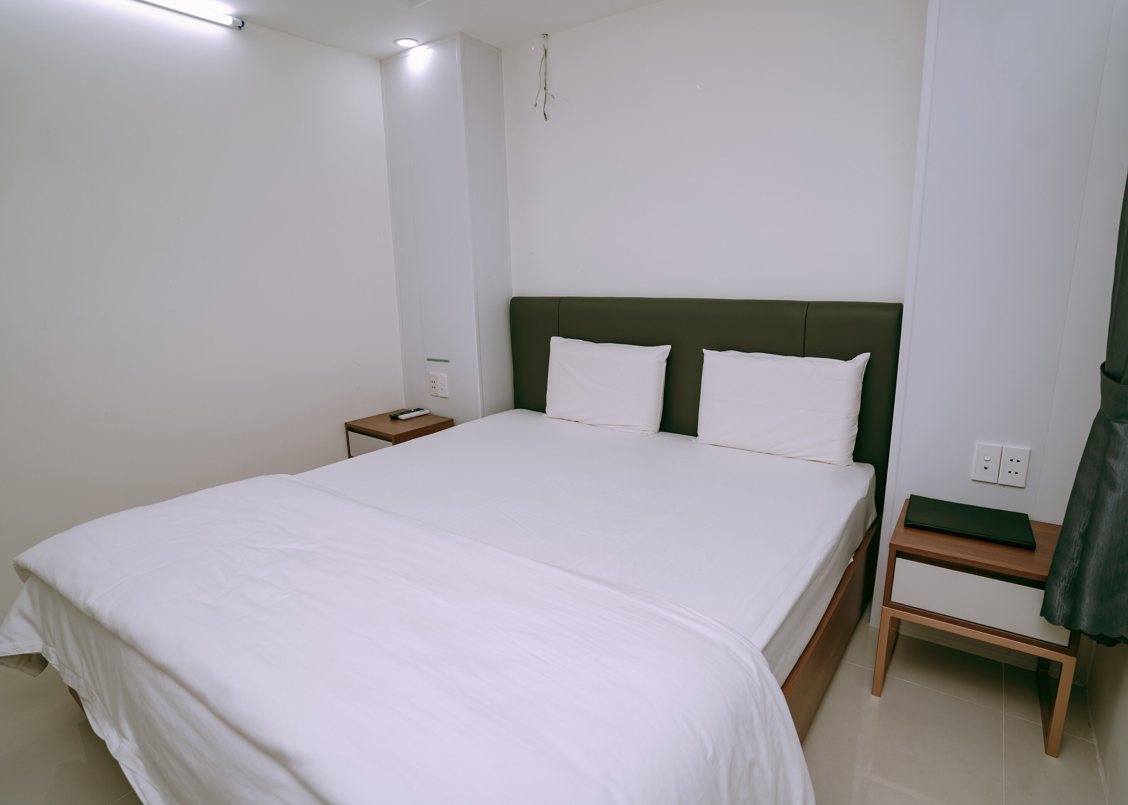 A neatly made bed with white linens, a green headboard, and a bedside table with a remote control.