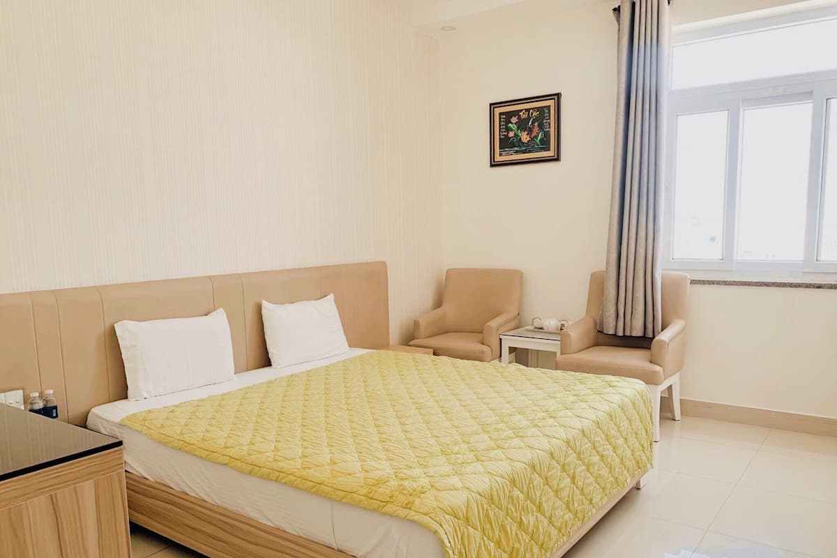 Een hotelkamer met een groot bed, twee fauteuils, een kleintje tafeltje met een theepot, en een lijst aan de muur.