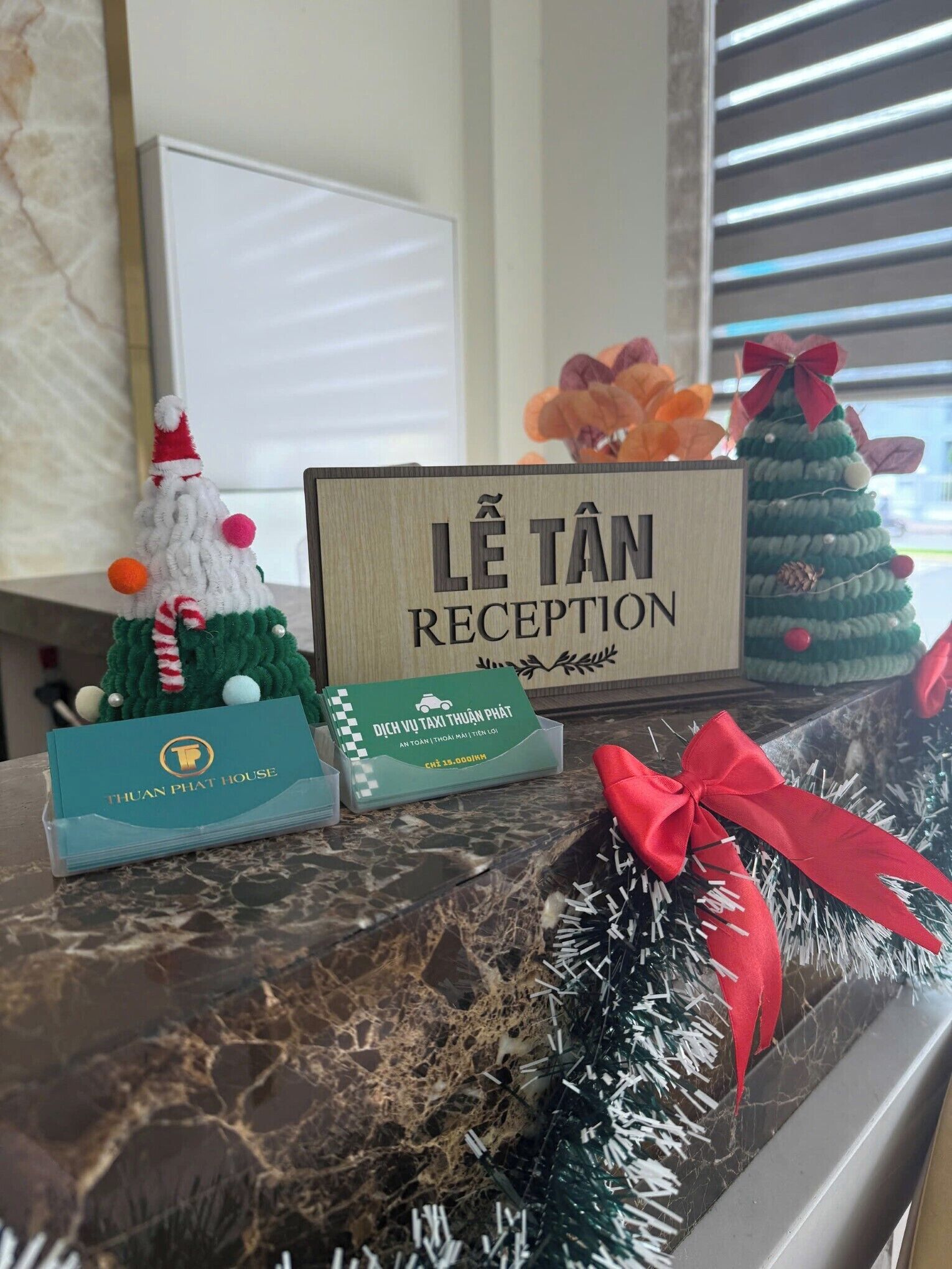 A reception desk with a sign reading "Lê Tân Reception" and a small Christmas tree decoration.