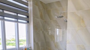 Une salle de bain avec une douche, des toilettes et une fenêtre équipée de stores.