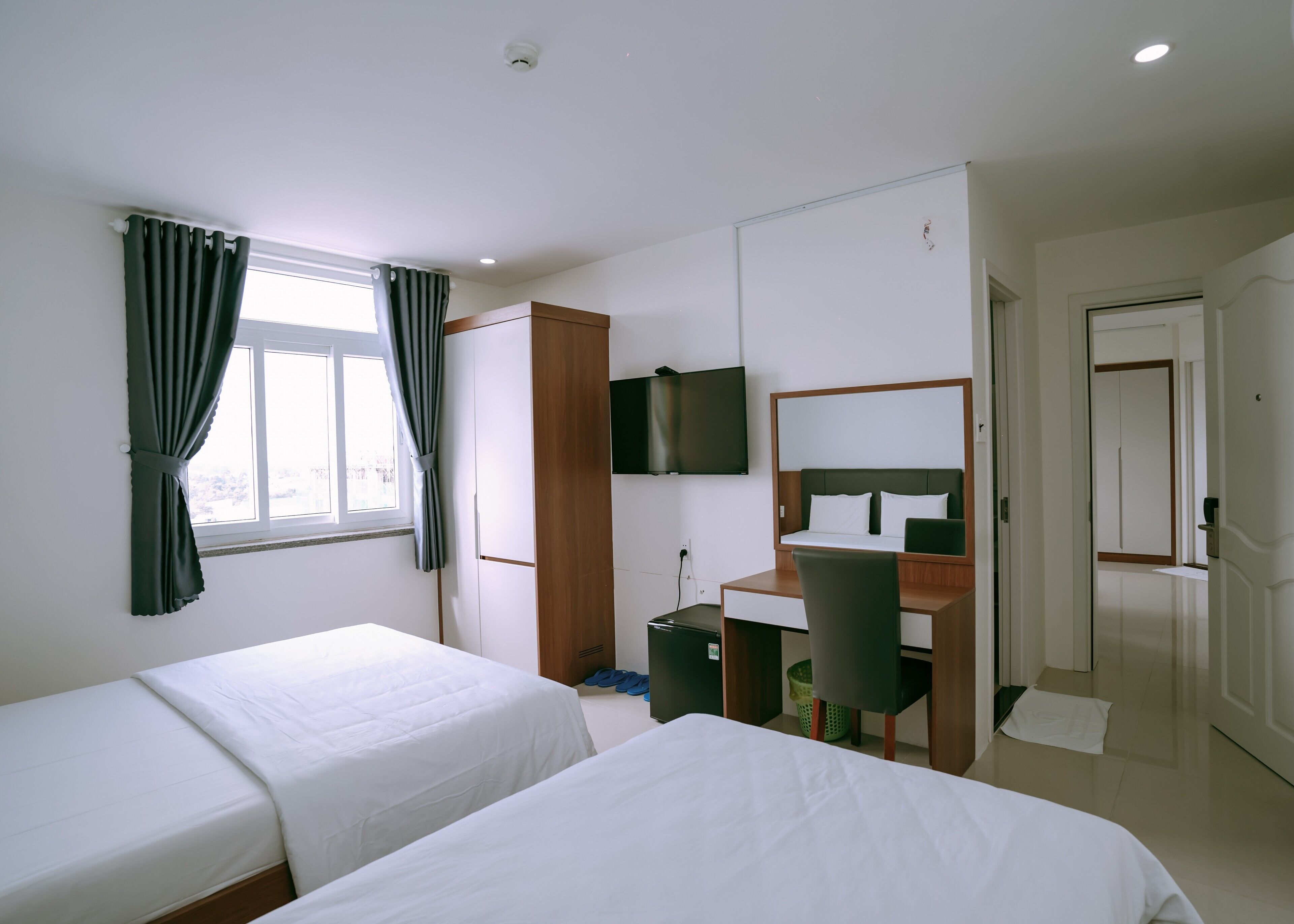 A hotel room with two beds, a desk, a chair, a TV, and a wardrobe.