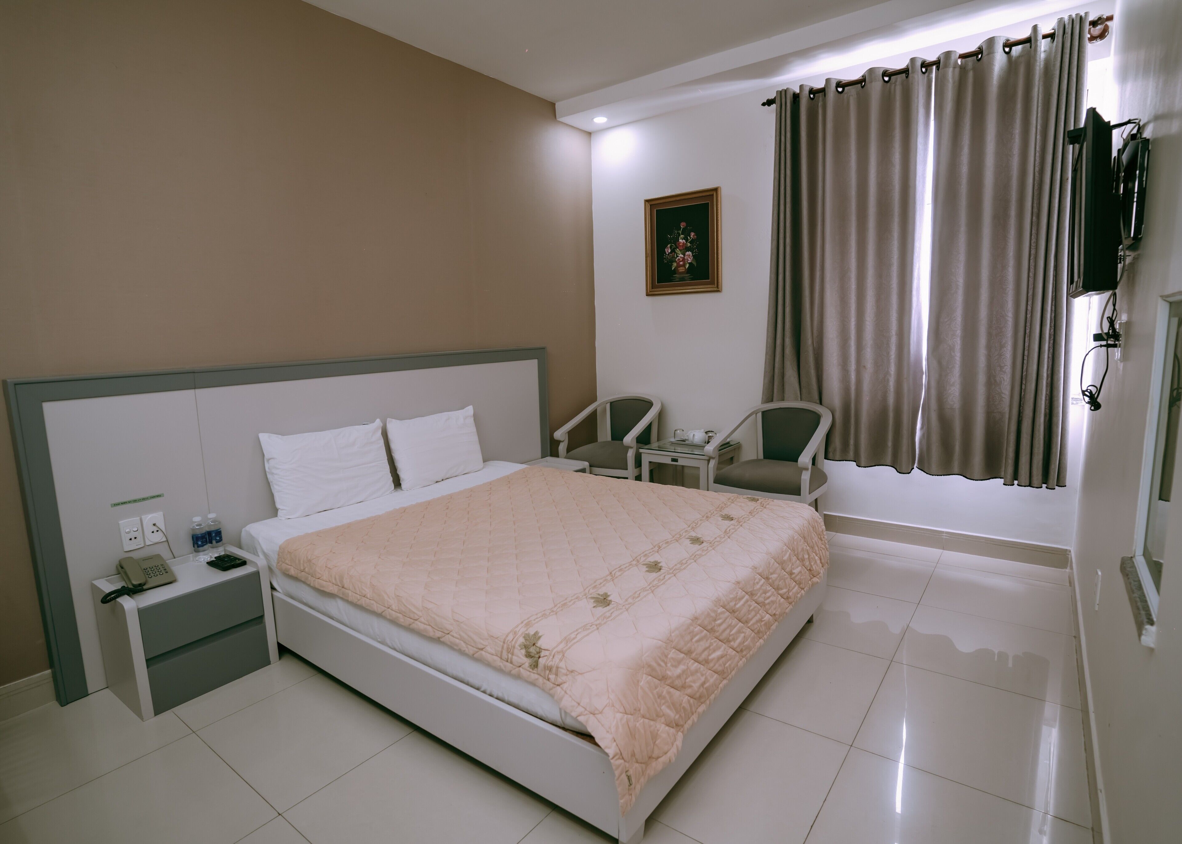 A hotel room with a bed, bedside table, chair, desk, and a TV mounted on the wall.