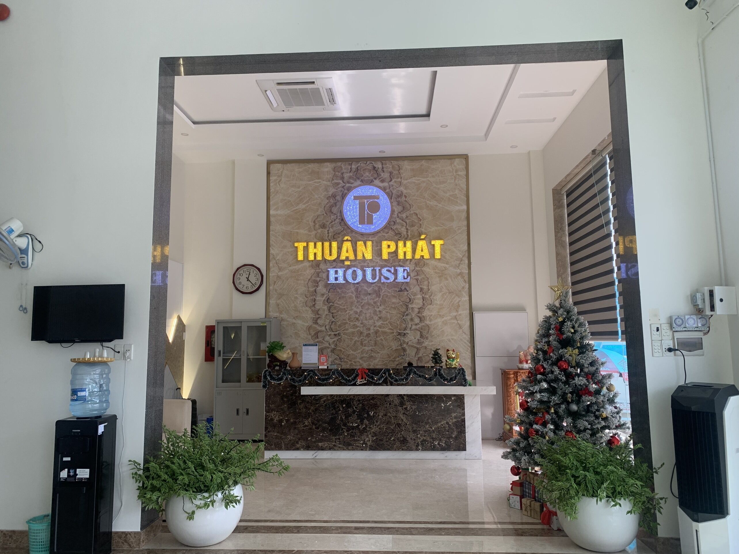 A hotel reception area with a marble wall, a clock, a water dispenser, and a Christmas tree.