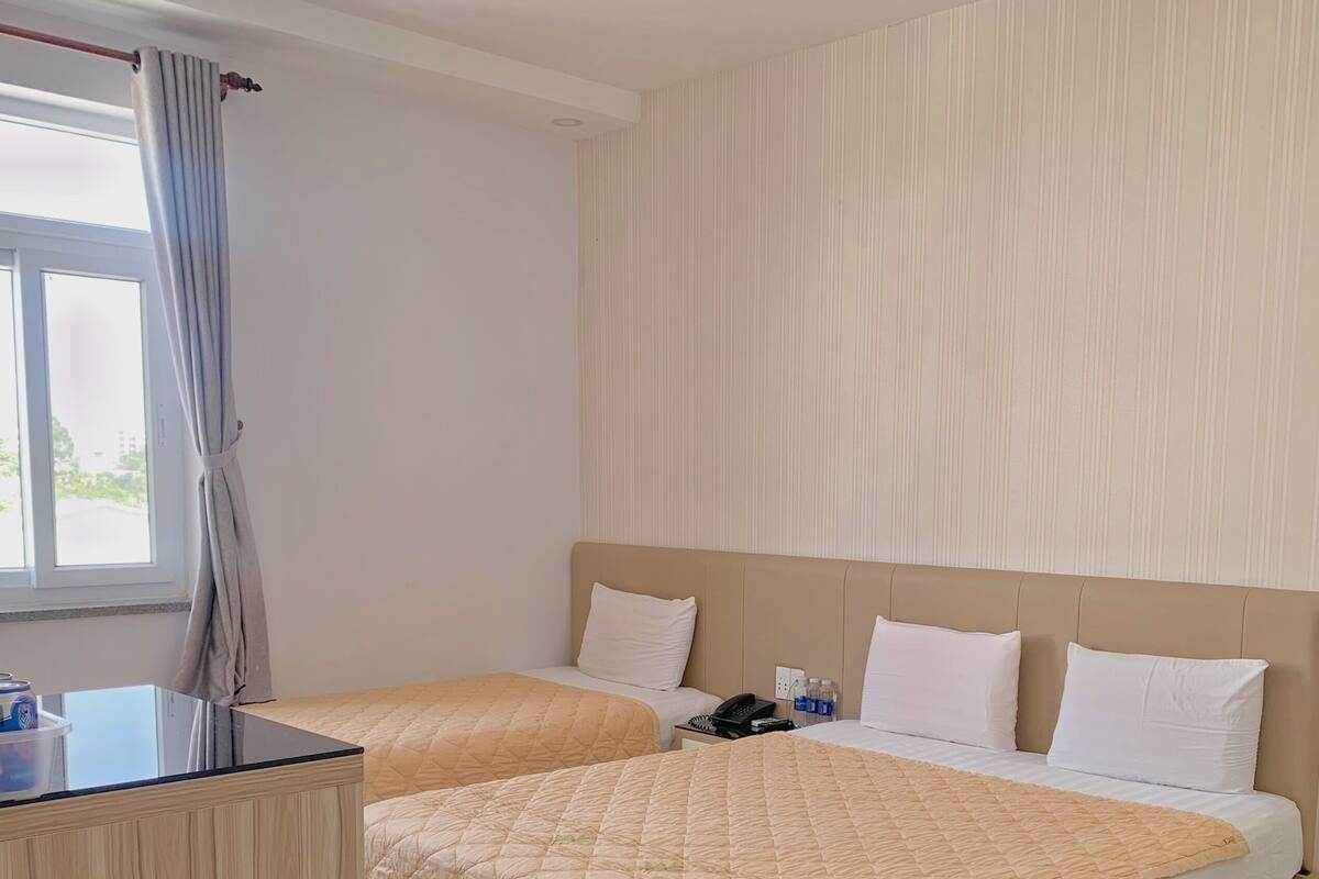 Een hotelkamer met twee bedden, een houten bureau, een telefoon en een raam met gordijnen.