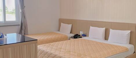 A hotel room with two beds, a wooden desk, a telephone, and a window with curtains.