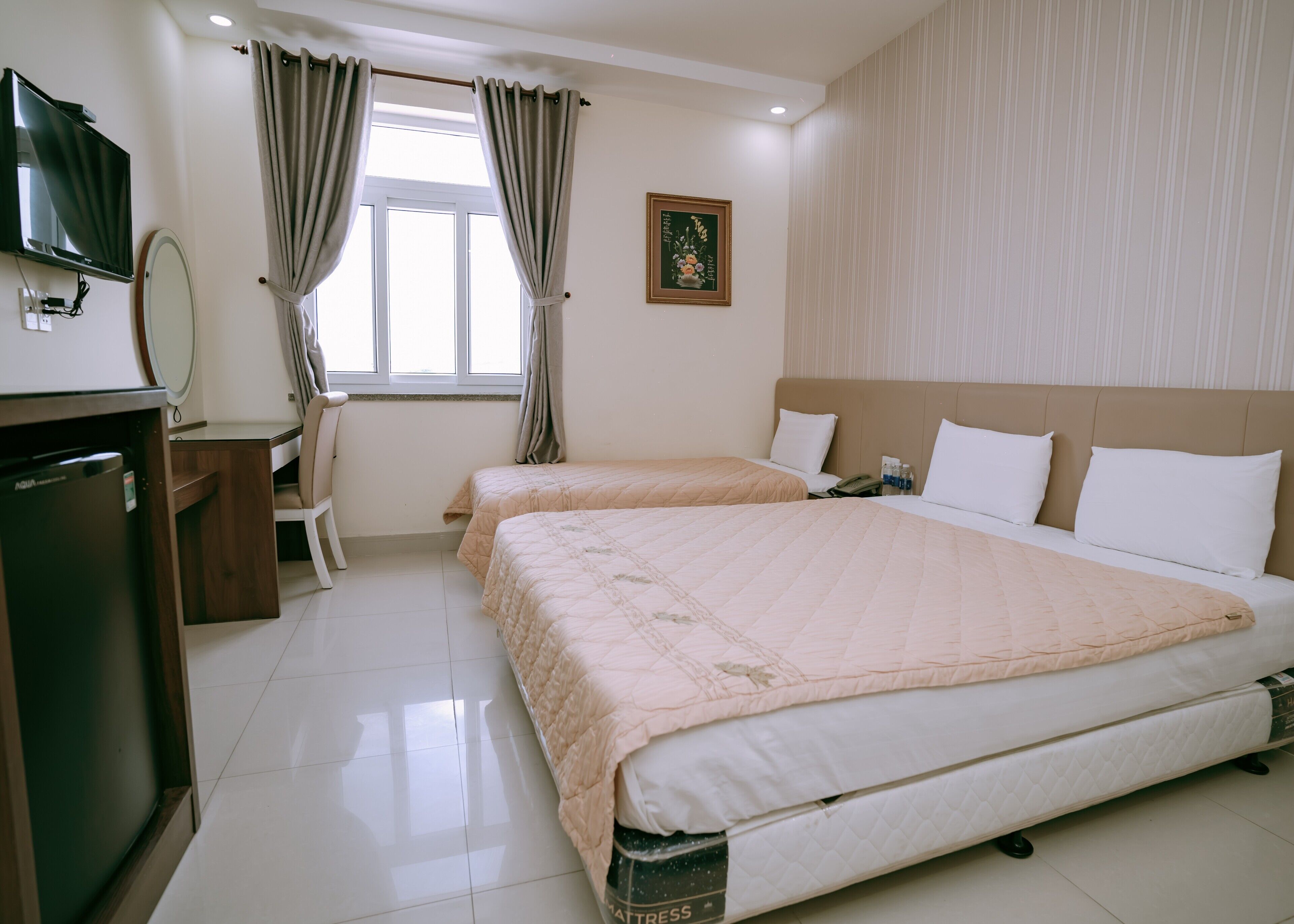 Habitación de hotel con dos camas, televisión, escritorio con silla, ventana con cortinas e imagen enmarcada en la pared.