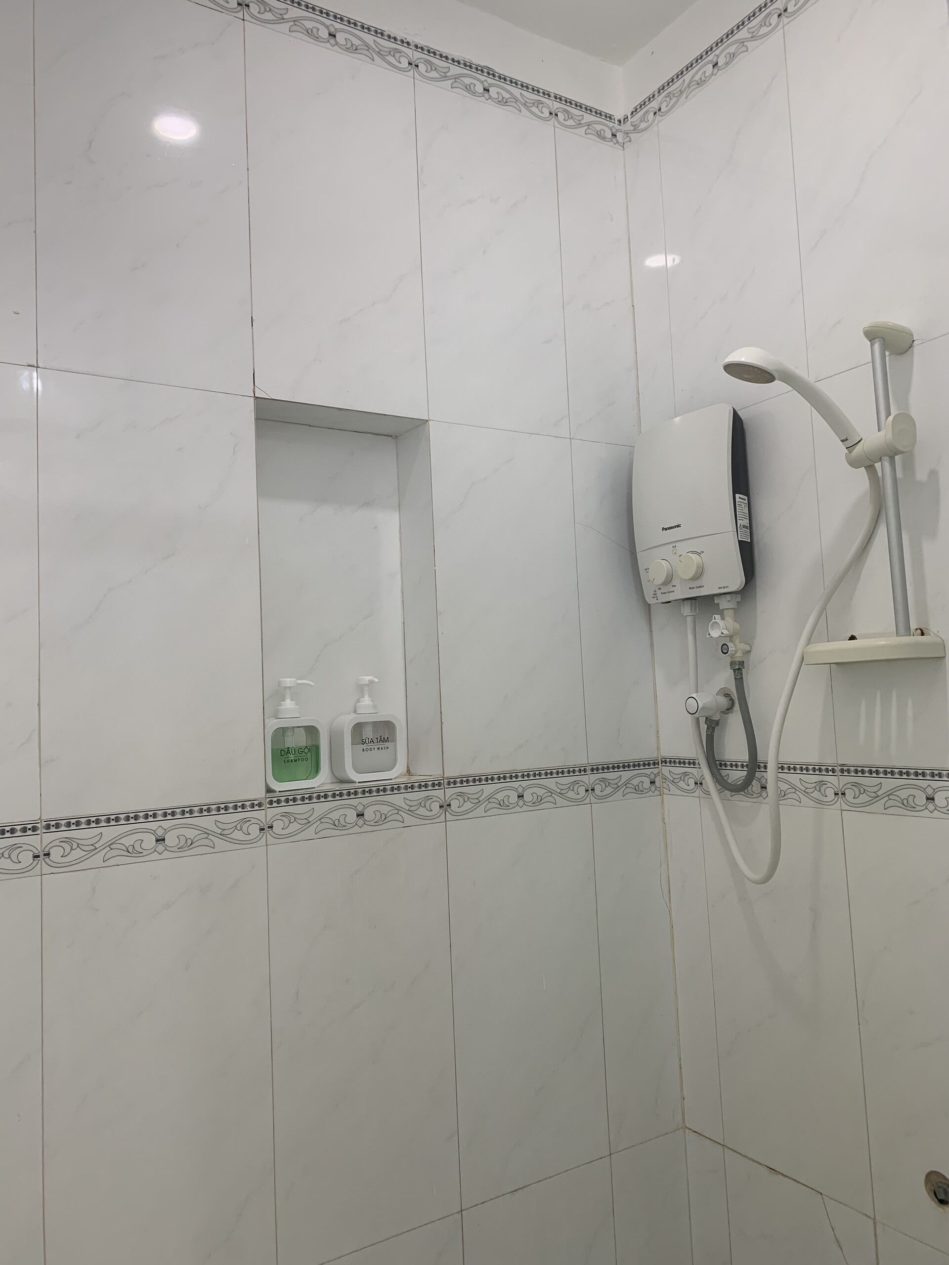 Un baño con azulejos blancos, ducha y dos botellas de champú y acondicionador.