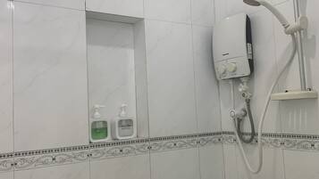 Un baño con azulejos blancos, ducha y dos botellas de champú y acondicionador.