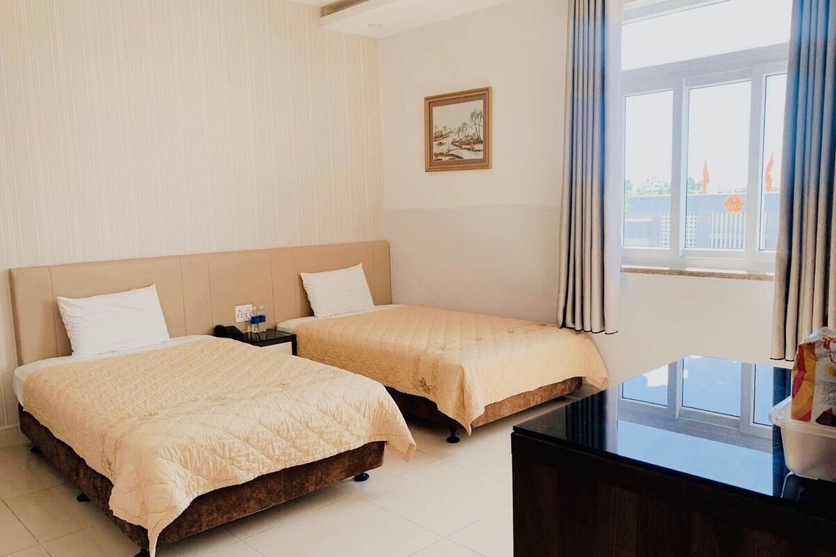 Een hotelkamer met twee bedden, een bureau en een raam met gordijnen.