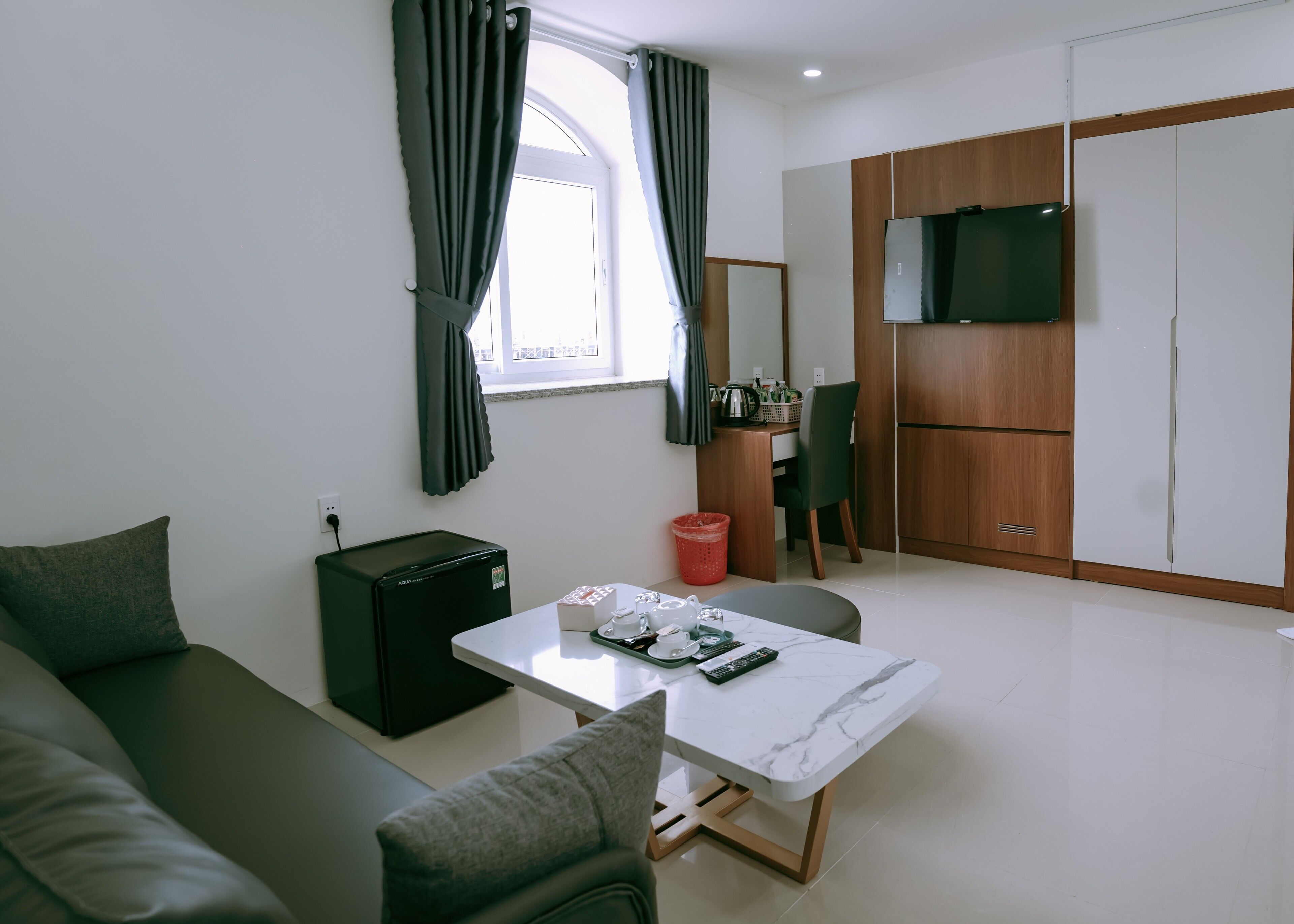 A modern living room with a sofa, a small table, a TV, and a kitchenette area.