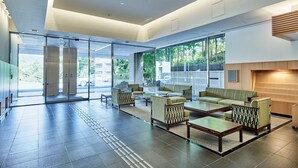 A spacious lobby with a modern design, featuring a seating area with sofas and armchairs, a reception desk, and large glass doors leading outside.