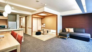 A modern hotel room with a kitchenette, a dining area, a seating area with a sofa, and a small table with a lamp.
