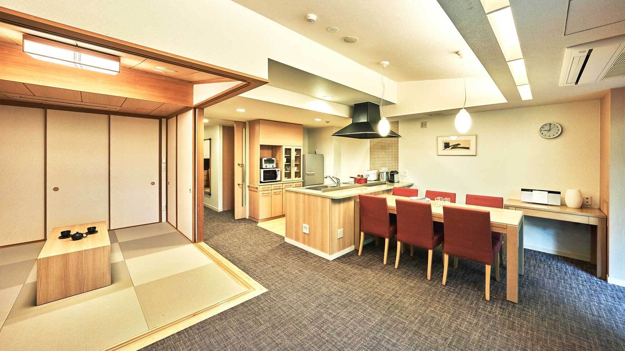 A modern kitchen with a central island, a dining area with red chairs, and a traditional tatami mat in the entrance.