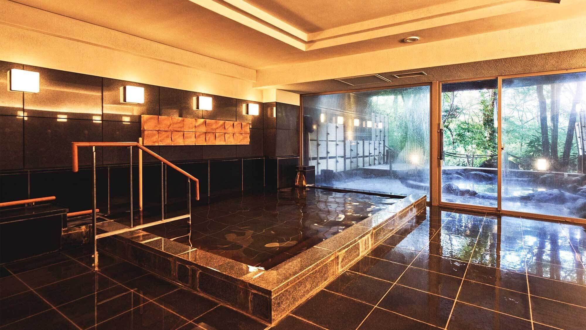 A modern indoor pool area with a glass wall providing a view of a forested outdoor area.