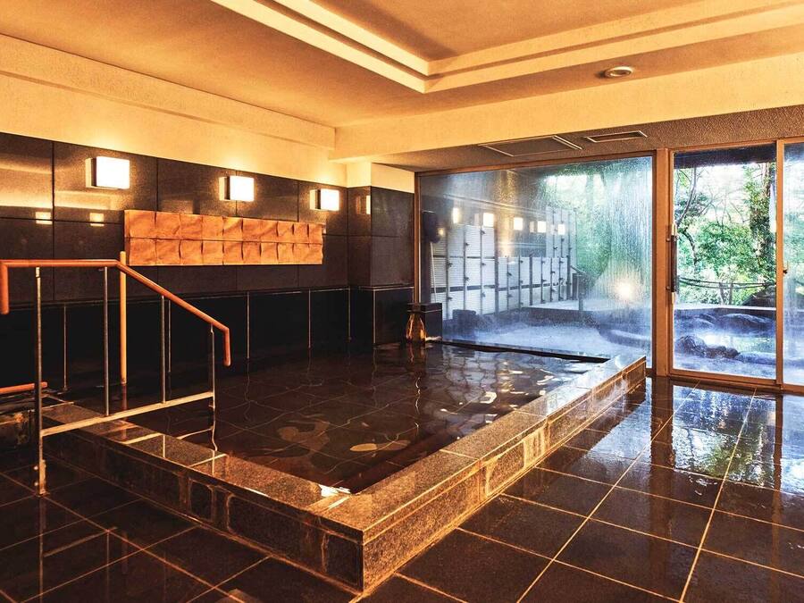 A modern indoor pool area with a glass wall providing a view of a forested outdoor area.