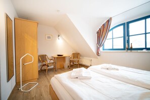 Ein Schlafzimmer mit Bett, zwei Stühlen, einem Schreibtisch, einem Heizkörper und einem Fenster mit Vorhängen.