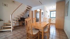 Un comedor con una mesa y sillas de madera, una escalera y una cocina al fondo.