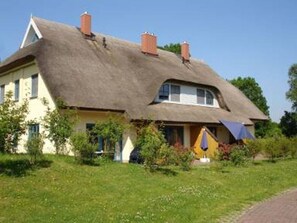 Una casa con techo de paja, un pequeño jardín y una chimenea visible.
