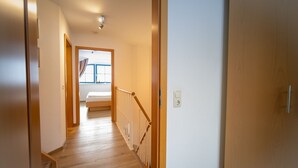 Un pasillo con suelo de madera que conduce a un dormitorio con cama y ventana.