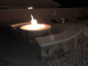 A stone fire pit with a wooden bench, surrounded by gravel and a brick wall. - The Watchman, Gateway to Zion - Hot Tub // Fire Pit (La Verkin)