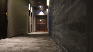 Un pasillo estrecho con piso alfombrado, una puerta de madera al final y una pared de ladrillo a la derecha.