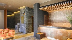 Zona de recepción con pared de piedra, asientos en un banco de madera y mostrador de recepción con diseño de listones de madera.