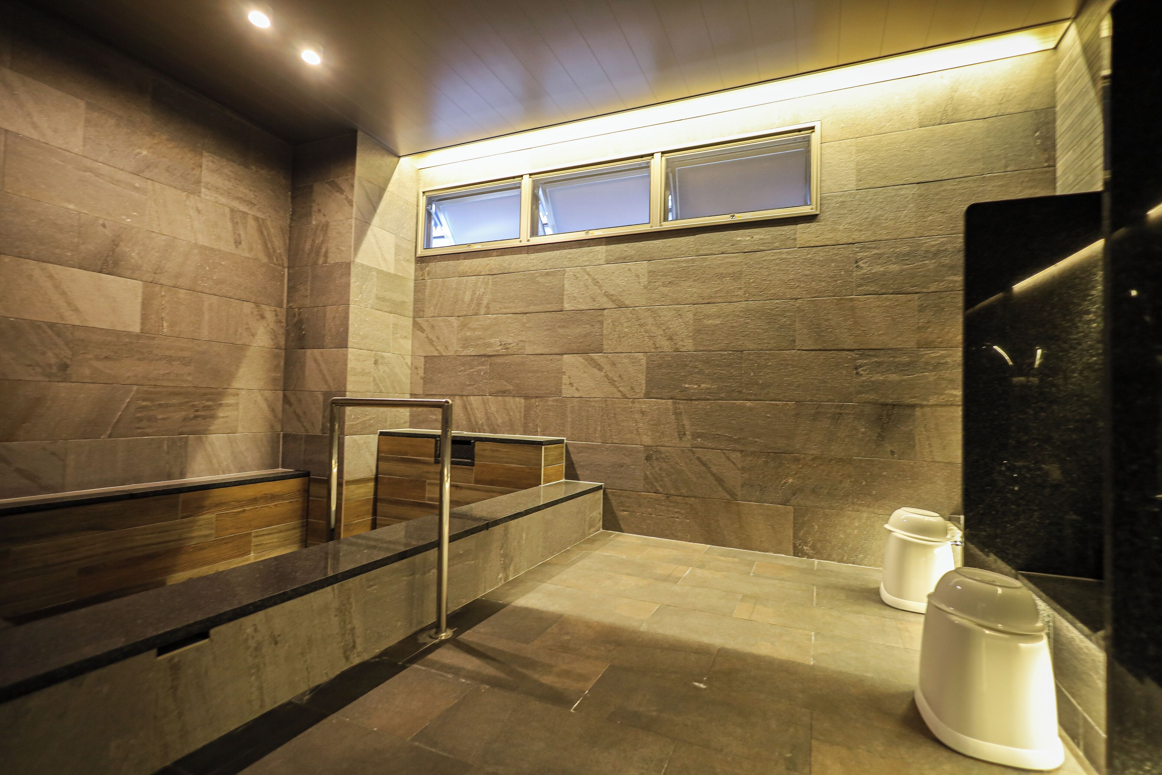 A modern bathroom with stone walls, a glass partition, and a metal handrail.