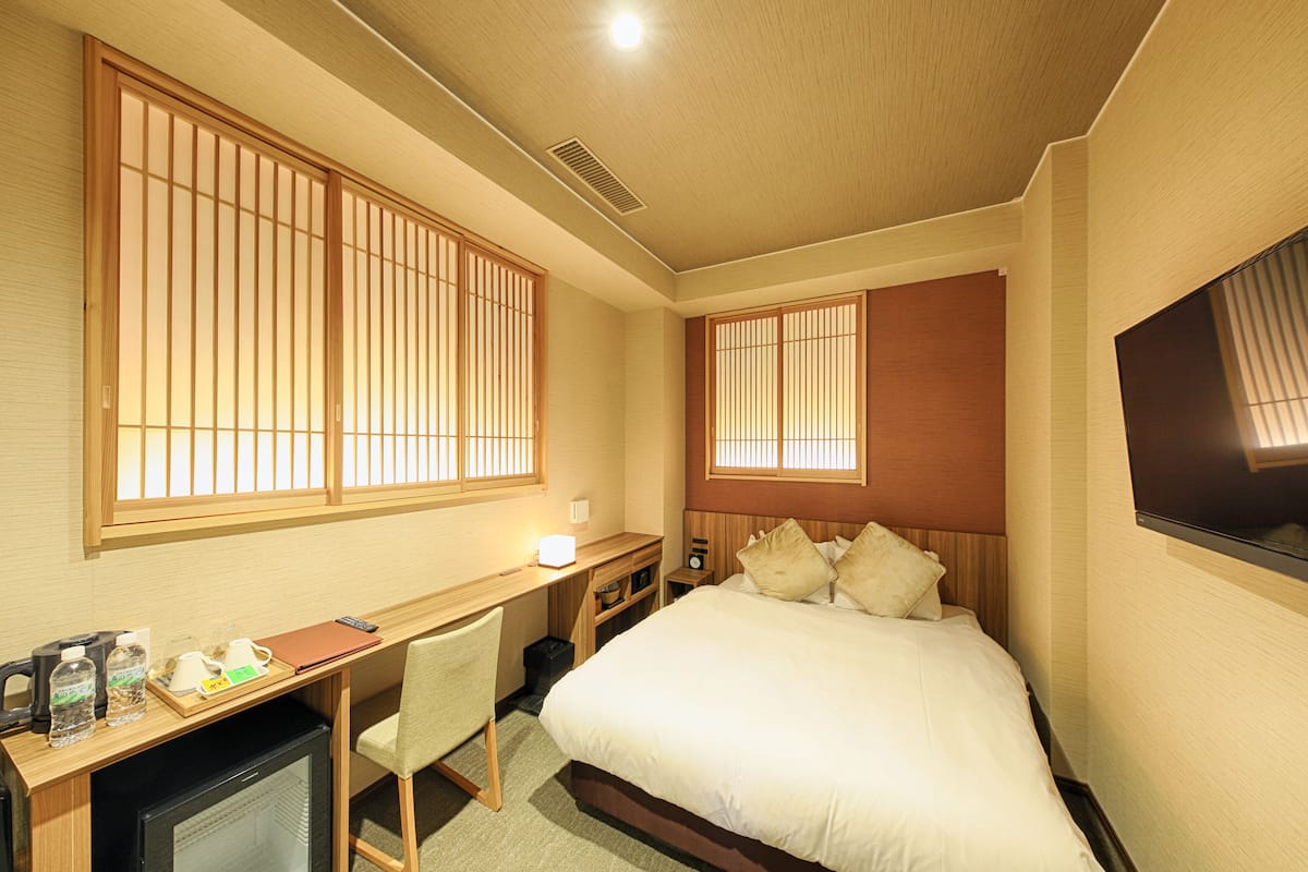 Una habitación de hotel con cama, escritorio, silla, televisión y ventanas.