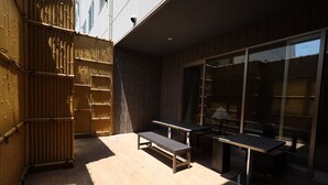 Un patio al aire libre con una mesa y banco de madera, cerramiento de bambú y una puerta de cristal que da a una habitación.