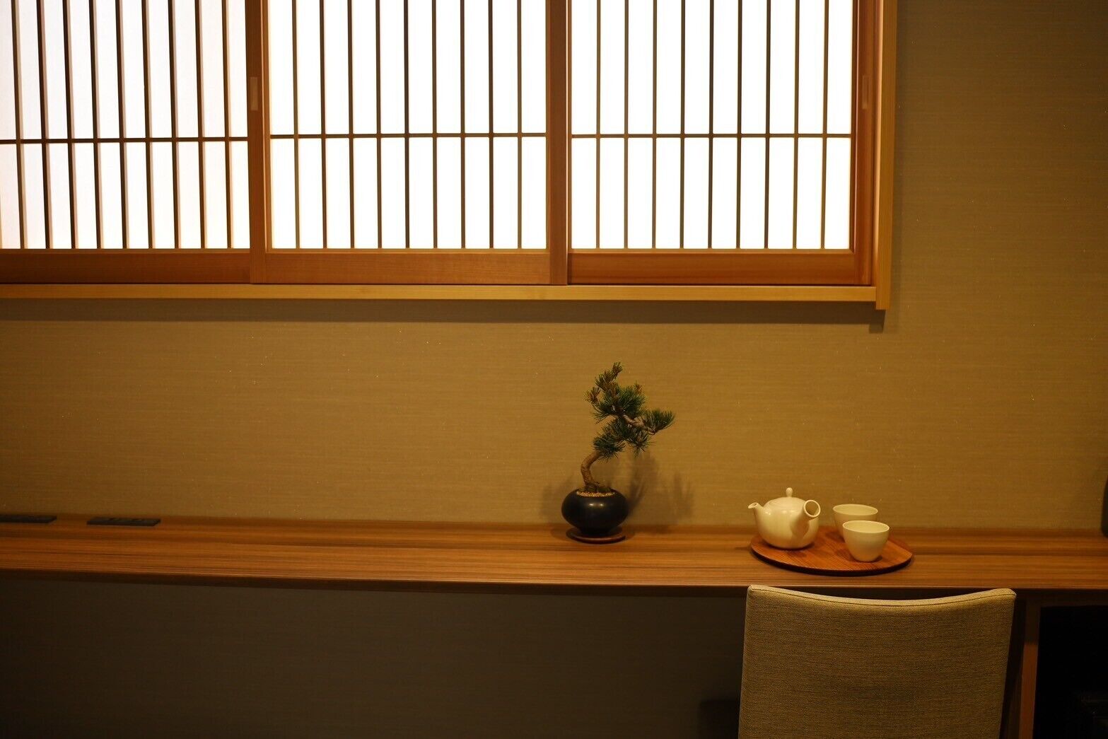 A room with a wooden desk, a bonsai tree, a teapot, and two cups.