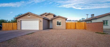 A single-story house with a garage, a wooden fence, and a gravel driveway.
