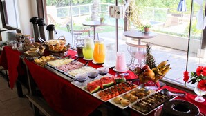 A buffet table with various food items and drinks, set up near a window with a view of the outdoors. - Pousada Villa Casablanca (Búzios)