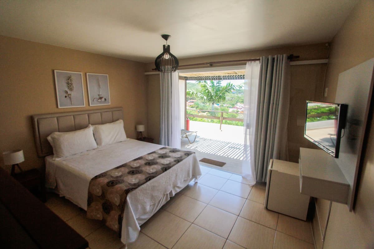 Habitación de hotel con cama, televisión y balcón con cortinas.