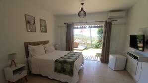 A bedroom with a bed, bedside table, lamp, air conditioning unit, and a TV. - Pousada Villa Casablanca (Búzios)