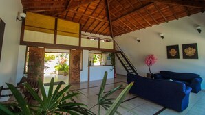 A spacious living area with a high wooden ceiling, a blue sofa, a staircase, and a reception desk. - Pousada Villa Casablanca (Búzios)