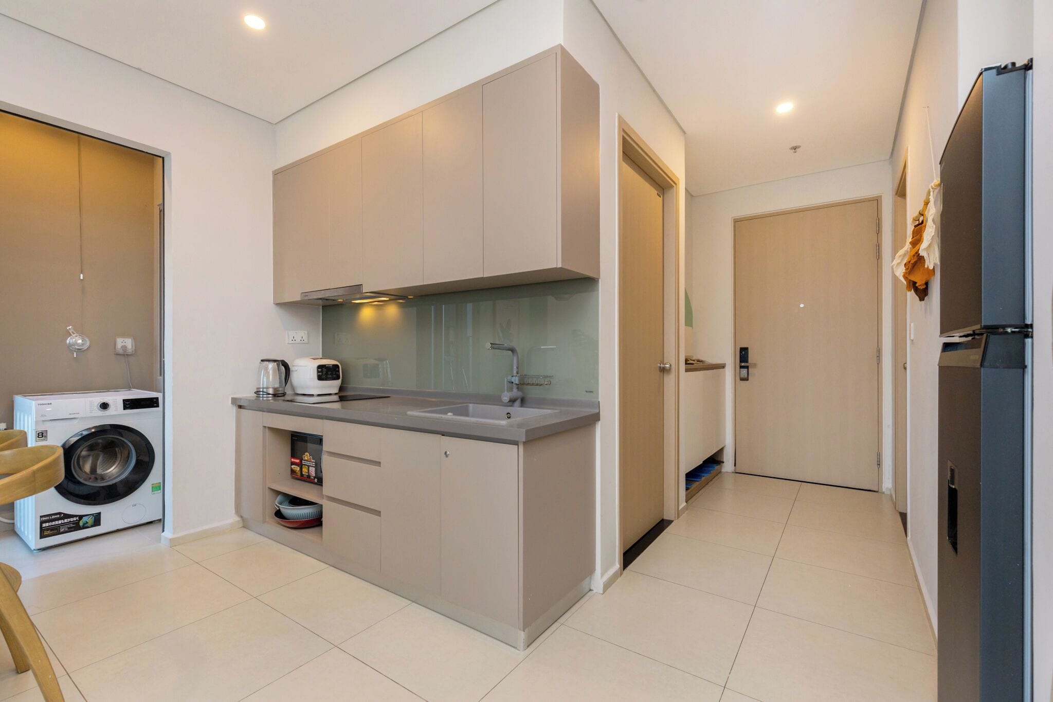 A compact kitchen with a washing machine, a coffee maker, and a refrigerator.
