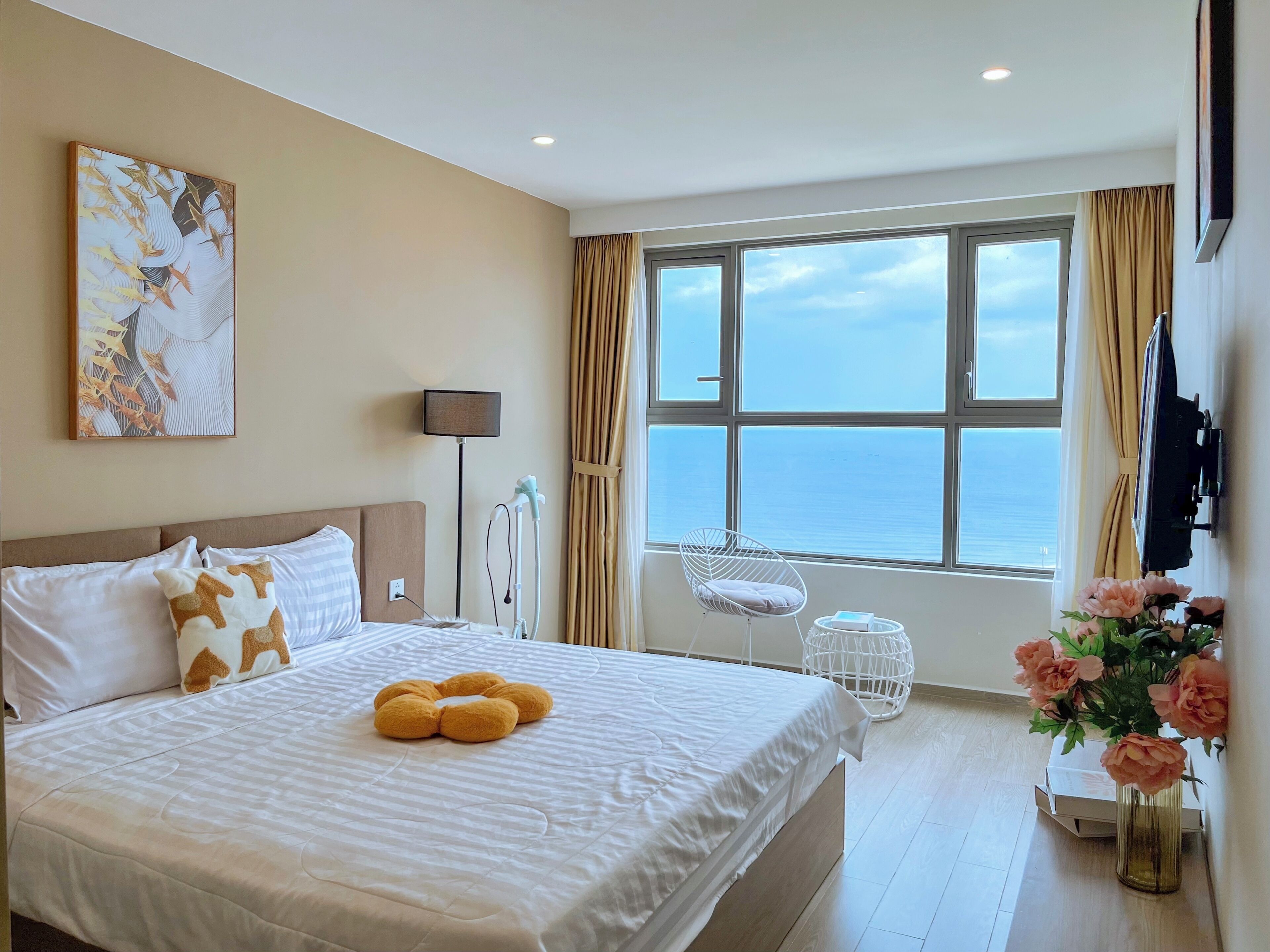 Habitación de hotel con una cama grande, una lámpara de noche, una silla, una ventana con vistas al mar y un cuadro en la pared.
