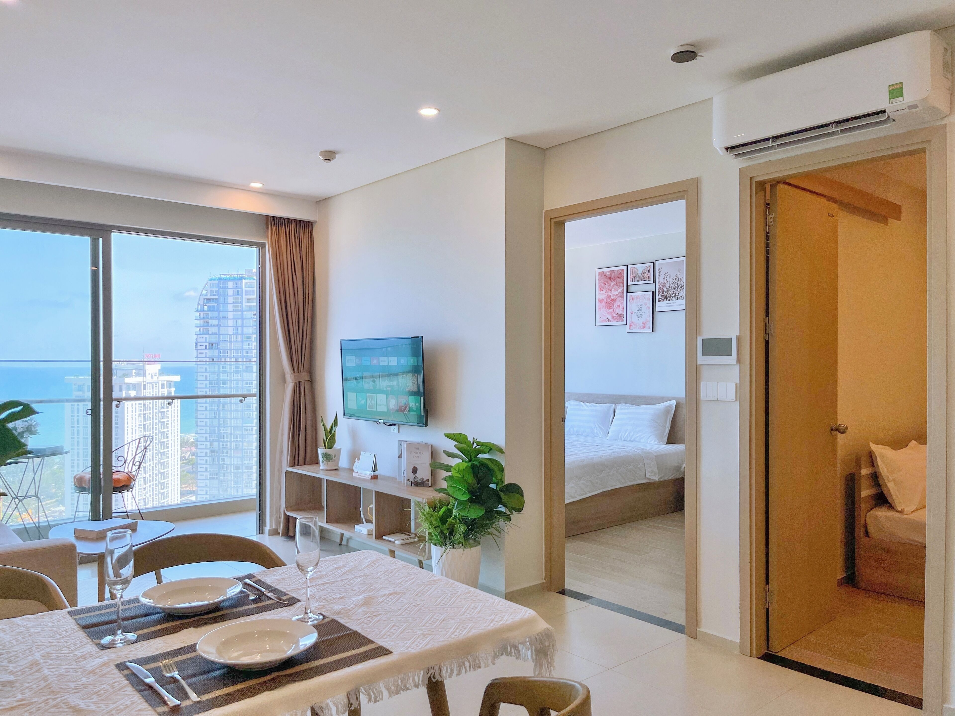 A modern hotel room with a balcony, a bed, a TV, and a dining area with a table set for two.