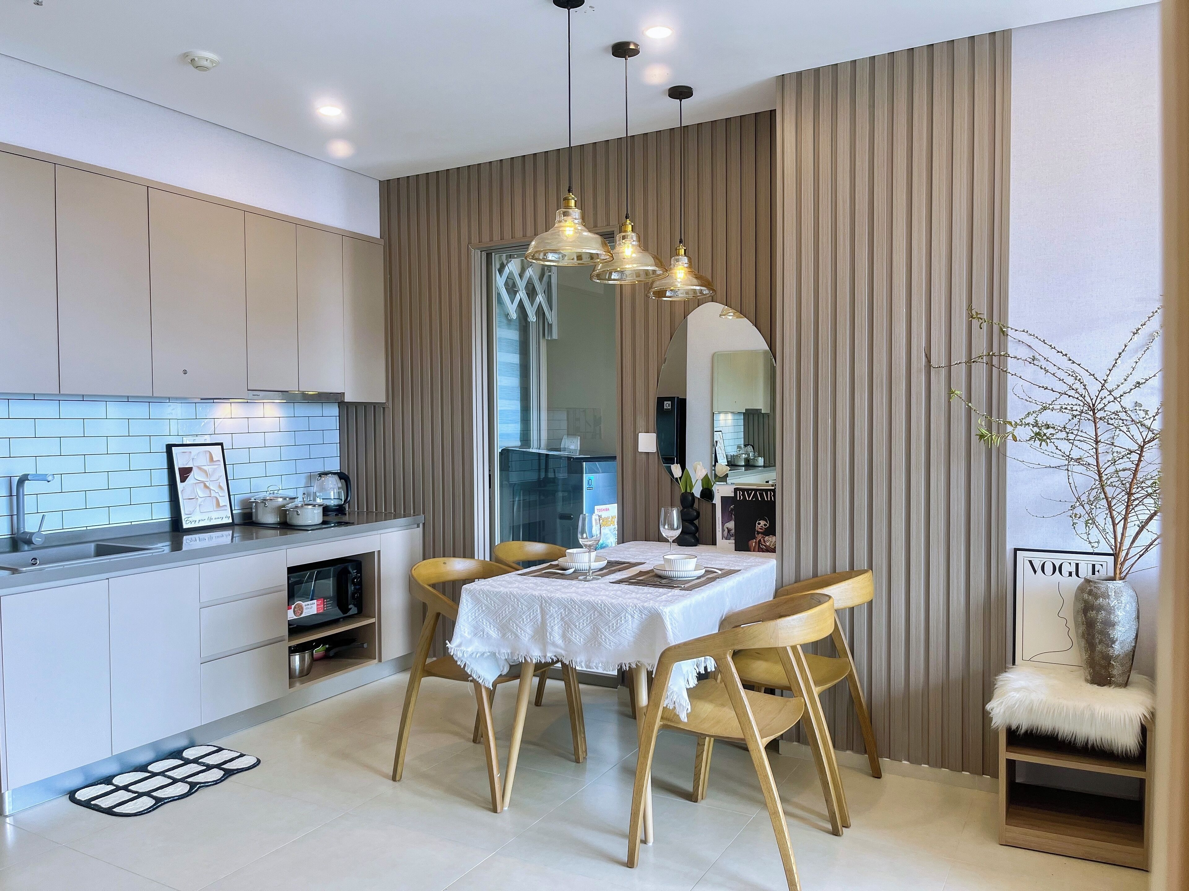 A modern kitchen with a dining area, featuring a kitchen island, pendant lighting, and a large mirror.
