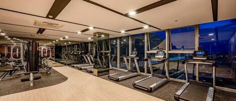 A gym with treadmills, weight machines, and a city view through large windows.